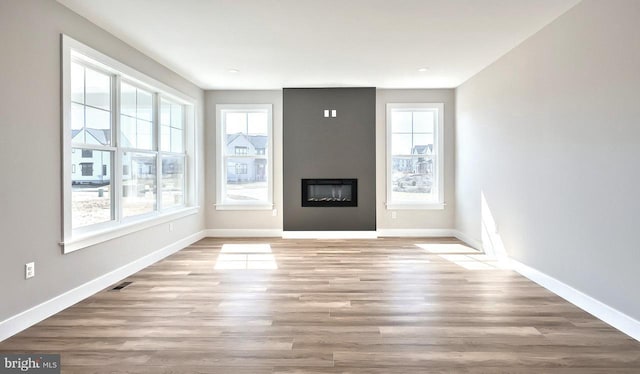 unfurnished living room with baseboards, a large fireplace, and wood finished floors