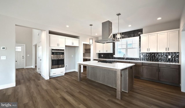 kitchen featuring tasteful backsplash, a center island, double oven, island range hood, and white cabinets