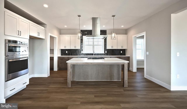 kitchen with island exhaust hood, a kitchen island, backsplash, white cabinetry, and appliances with stainless steel finishes