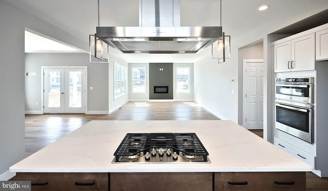 kitchen featuring light stone counters, wood finished floors, open floor plan, range hood, and stainless steel appliances