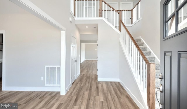 entrance foyer with visible vents, baseboards, stairway, a towering ceiling, and wood finished floors