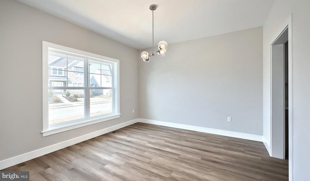 spare room featuring a notable chandelier, wood finished floors, and baseboards