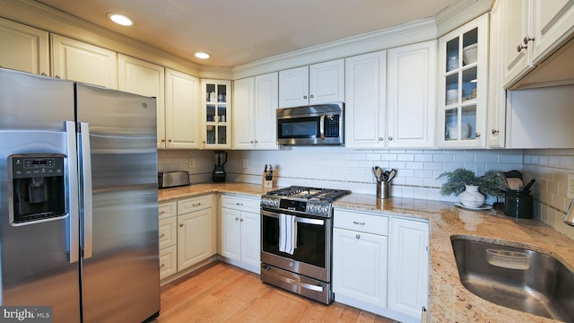 kitchen featuring light wood finished floors, backsplash, light stone counters, appliances with stainless steel finishes, and a sink