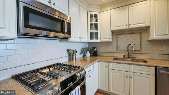 kitchen with a sink, tasteful backsplash, appliances with stainless steel finishes, glass insert cabinets, and light stone countertops