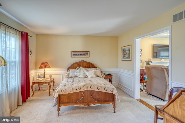 bedroom featuring wainscoting, visible vents, and light colored carpet