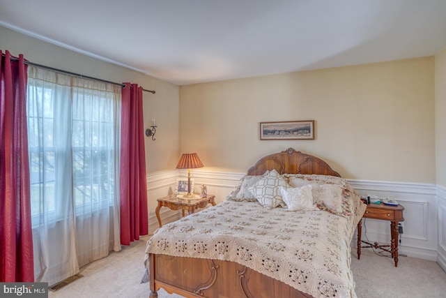 bedroom with a wainscoted wall, light colored carpet, visible vents, and a decorative wall