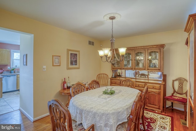 dining room featuring a notable chandelier, baseboards, visible vents, and light wood finished floors