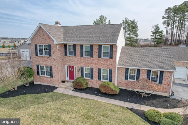 colonial home with a front yard, brick siding, roof with shingles, and a chimney