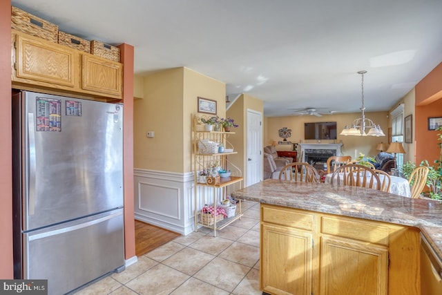 kitchen featuring stainless steel appliances, wainscoting, a fireplace, light tile patterned floors, and hanging light fixtures