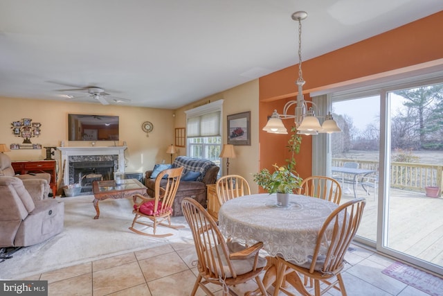 dining space with light tile patterned floors, ceiling fan with notable chandelier, and a premium fireplace