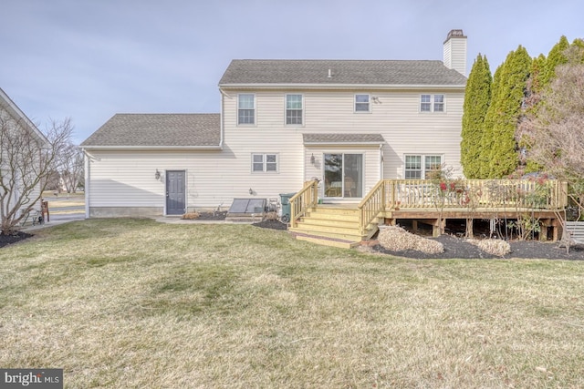 back of property featuring a chimney, a lawn, a wooden deck, and roof with shingles