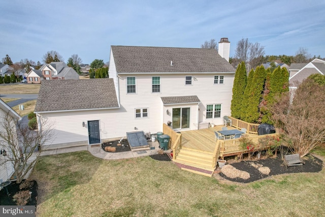 rear view of property with a yard, roof with shingles, a deck, and a chimney