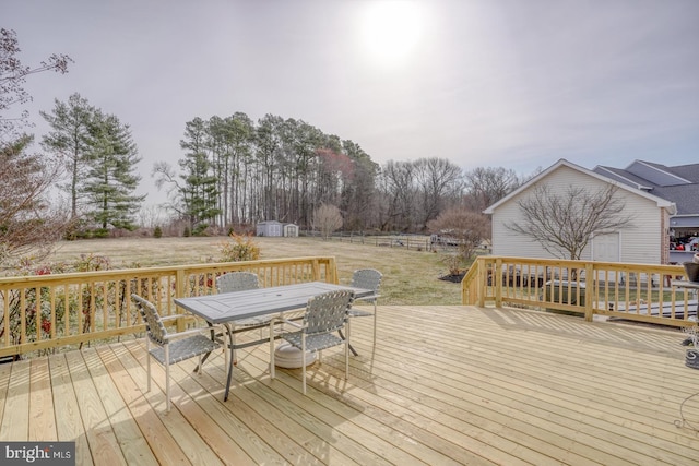 wooden terrace featuring an outbuilding, outdoor dining space, a storage shed, and fence