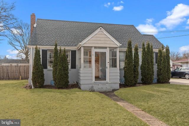 bungalow-style house with a front yard, a shingled roof, a chimney, and fence