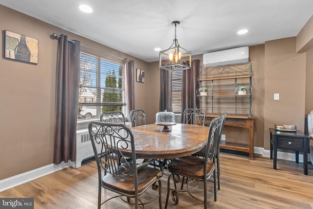 dining room with a wall mounted air conditioner, a chandelier, baseboards, and light wood-style flooring