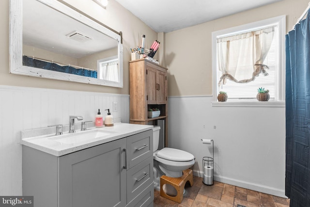 full bathroom with vanity, visible vents, a wainscoted wall, stone finish floor, and toilet