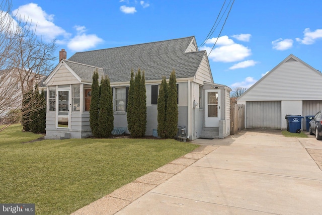 view of front of house featuring an outbuilding, a chimney, a front lawn, and a shingled roof