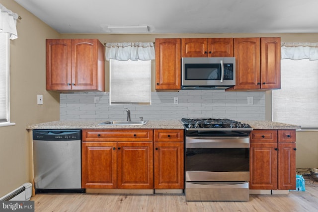 kitchen with a sink, light wood-type flooring, a baseboard radiator, and stainless steel appliances