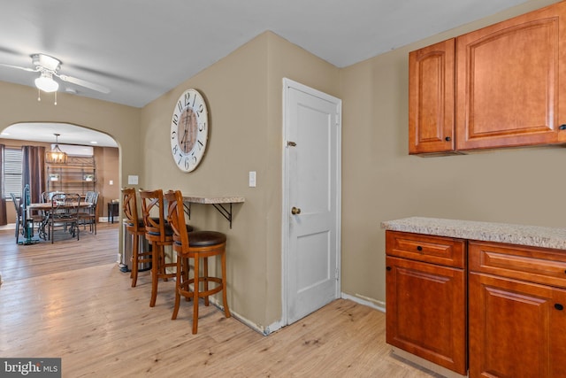 kitchen featuring light wood-style flooring, a ceiling fan, arched walkways, brown cabinetry, and baseboards