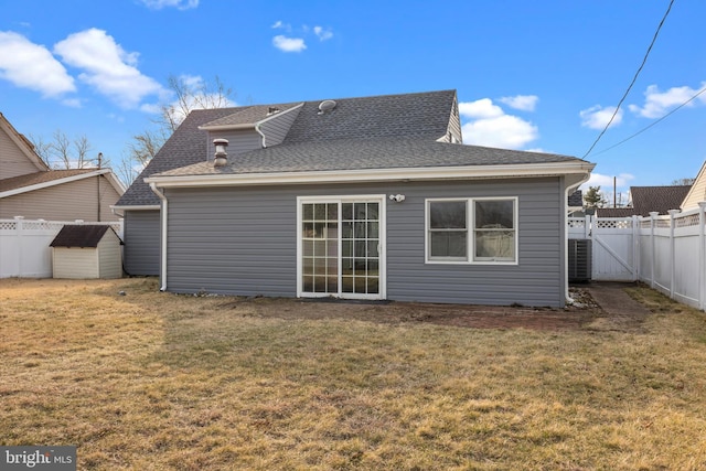 back of property featuring an outdoor structure, a lawn, a fenced backyard, and roof with shingles