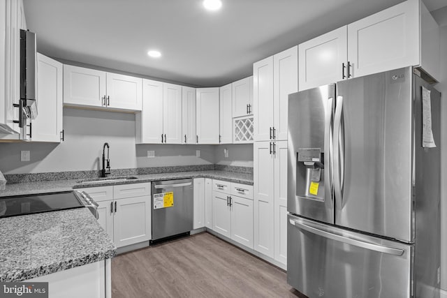 kitchen featuring white cabinetry, stainless steel appliances, light wood-style floors, and a sink