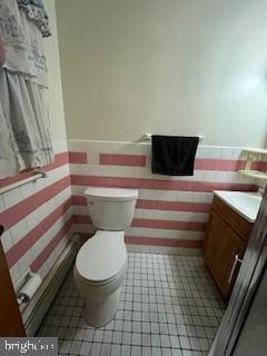 half bathroom with tile patterned floors, a wainscoted wall, toilet, and vanity