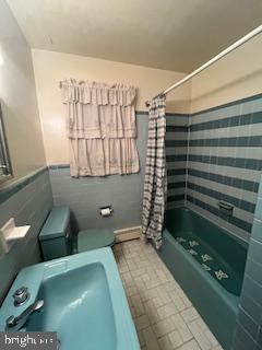 full bath with a wainscoted wall, shower / bath combo with shower curtain, toilet, and tile walls