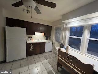 kitchen with light tile patterned floors, white appliances, dark brown cabinetry, and light countertops