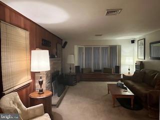 living area featuring light colored carpet, visible vents, and wood walls