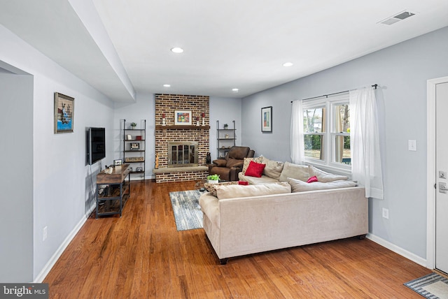 living room featuring wood finished floors, a fireplace, visible vents, and baseboards