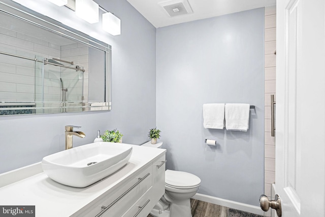 full bathroom with visible vents, toilet, wood finished floors, tiled shower, and vanity