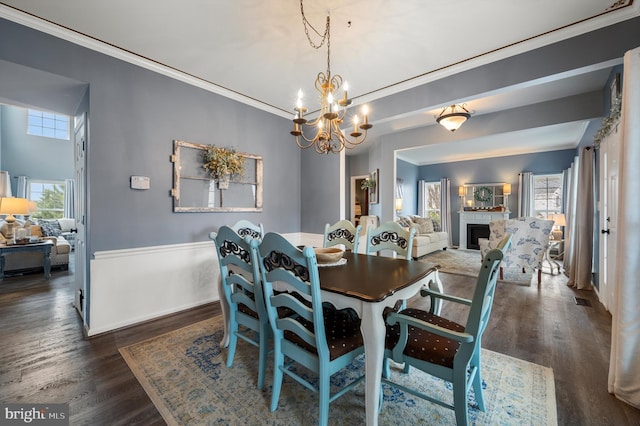 dining space featuring a notable chandelier, dark wood-type flooring, a fireplace, and crown molding