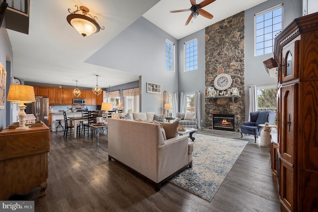 living area featuring dark wood-style floors, a stone fireplace, ceiling fan, and a towering ceiling