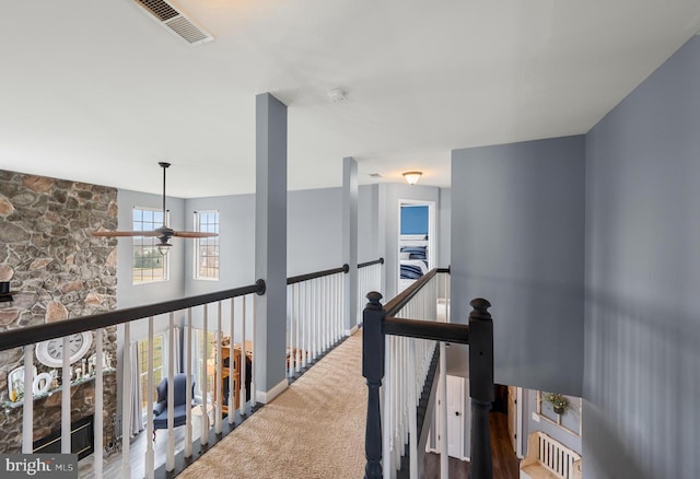 hall with an upstairs landing, visible vents, and carpet flooring