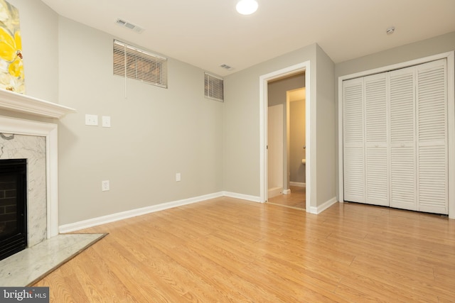 unfurnished living room featuring a high end fireplace, visible vents, baseboards, and wood finished floors