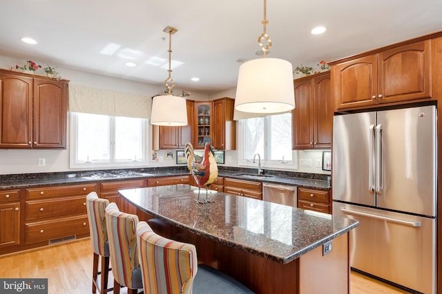 kitchen featuring brown cabinetry, a kitchen bar, a sink, dark stone countertops, and stainless steel appliances