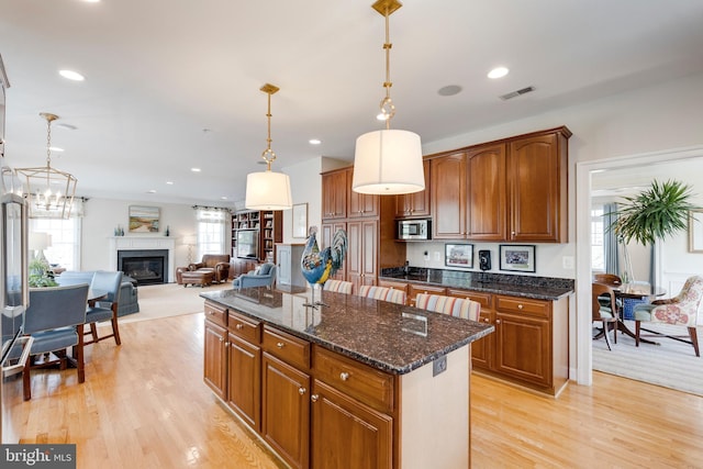 kitchen with light wood-style floors, a center island, hanging light fixtures, stainless steel microwave, and a glass covered fireplace