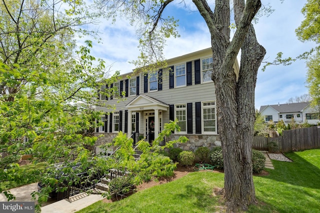colonial home featuring a front yard, fence, and stone siding