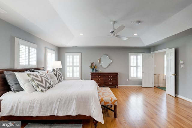 bedroom with a tray ceiling, multiple windows, and light wood-type flooring