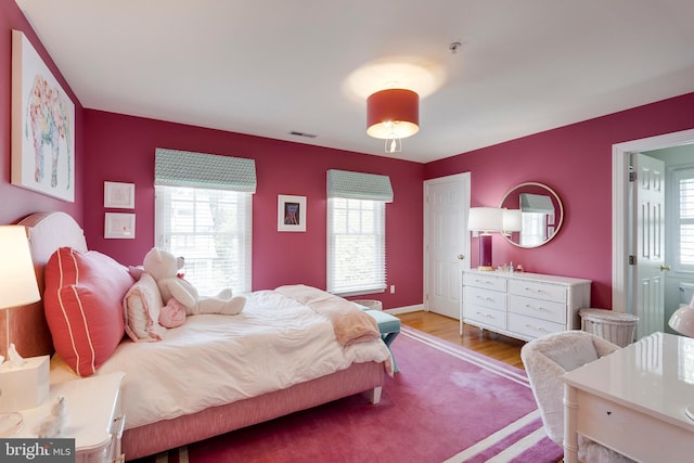 bedroom with baseboards, visible vents, multiple windows, and wood finished floors