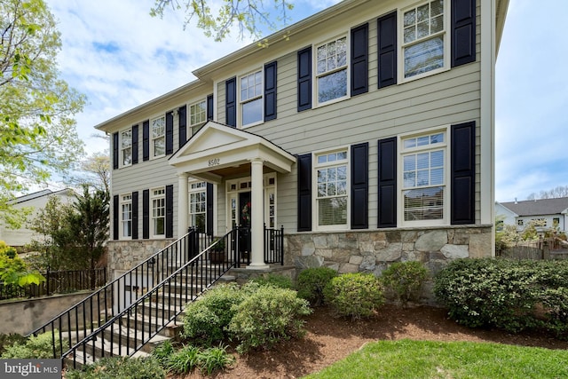 colonial house featuring fence and stone siding