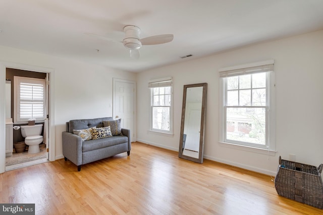 living area featuring ceiling fan, visible vents, baseboards, and light wood finished floors