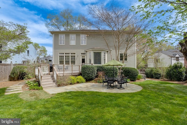 rear view of house with fence, a wooden deck, a lawn, and a patio area