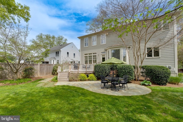back of property featuring a lawn, fence, a wooden deck, and a patio area