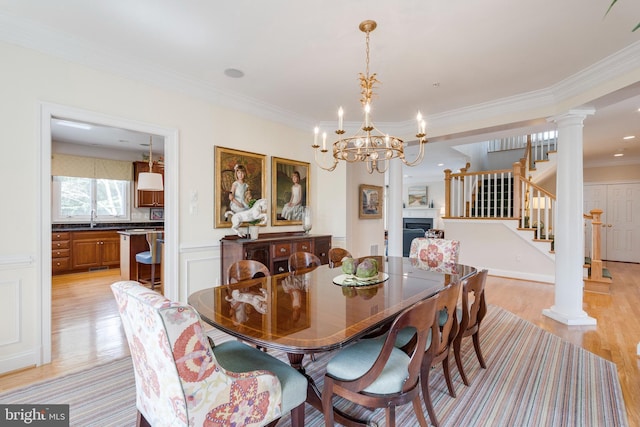 dining room featuring crown molding, an inviting chandelier, light wood-style flooring, ornate columns, and stairway
