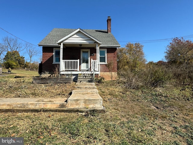 bungalow featuring brick siding, covered porch, a chimney, and a shingled roof