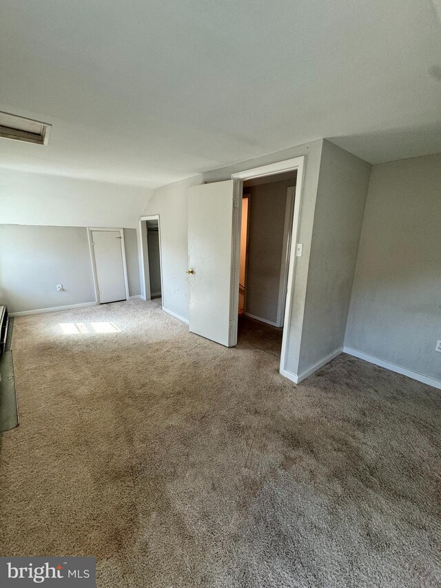 carpeted empty room with vaulted ceiling, attic access, visible vents, and baseboards