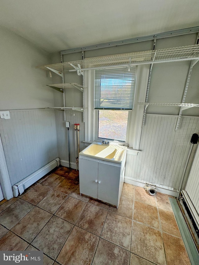 laundry room with a baseboard heating unit, a wainscoted wall, tile patterned floors, cabinet space, and a sink