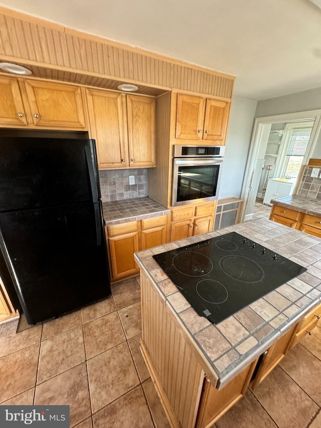 kitchen featuring tasteful backsplash, light tile patterned floors, tile countertops, and black appliances