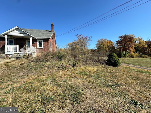 view of property exterior with brick siding, covered porch, and a chimney